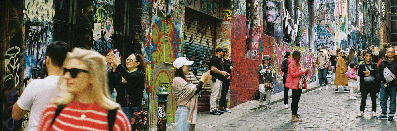 People walking and taking photos of a heavily graffitied alleyway in Melbourne.