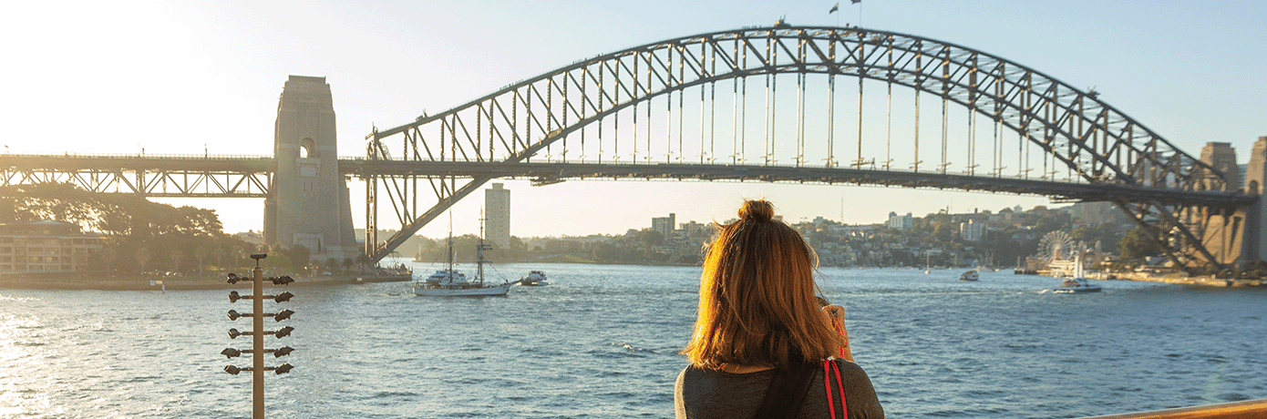 A woman on a boat in the Sydney Harbour taking a photo of the Sydney Harbour bridge.