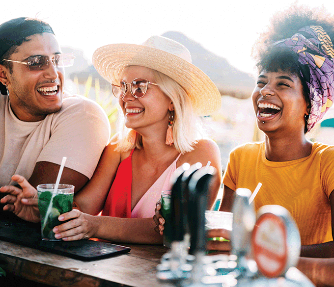Three friends laughing at a bar with drinks.