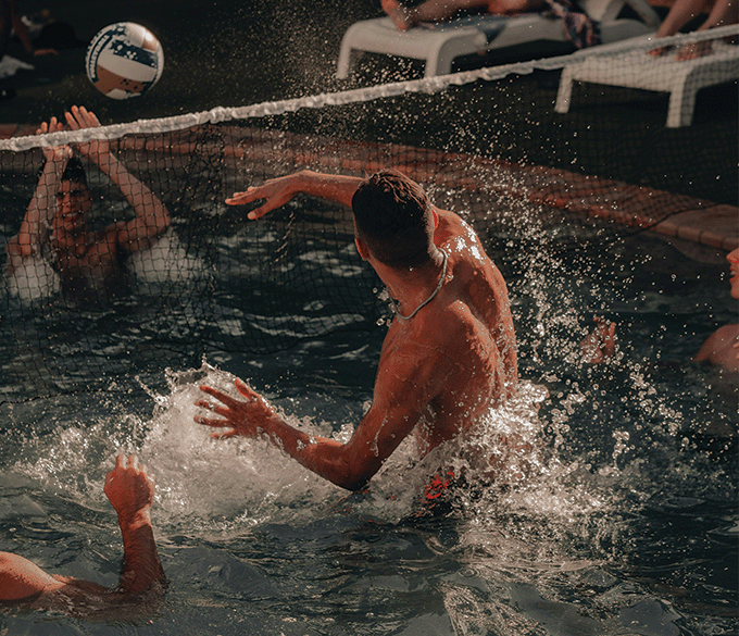 Man jumping out of pool water while playing volleyball.