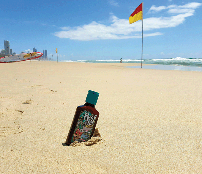 Sun tan oil wedged in the sand in front of surf flags on a Gold Coast beach.