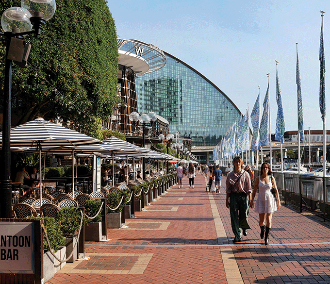A couple hold hands walking along the Sydney city waterfront.