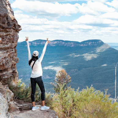 Woman overlooking a mountain range holding up two peace signs.