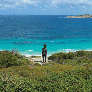 A person stands on rocks close to the blue ocean.