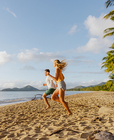 Happy couple running down a North Queensland beach.